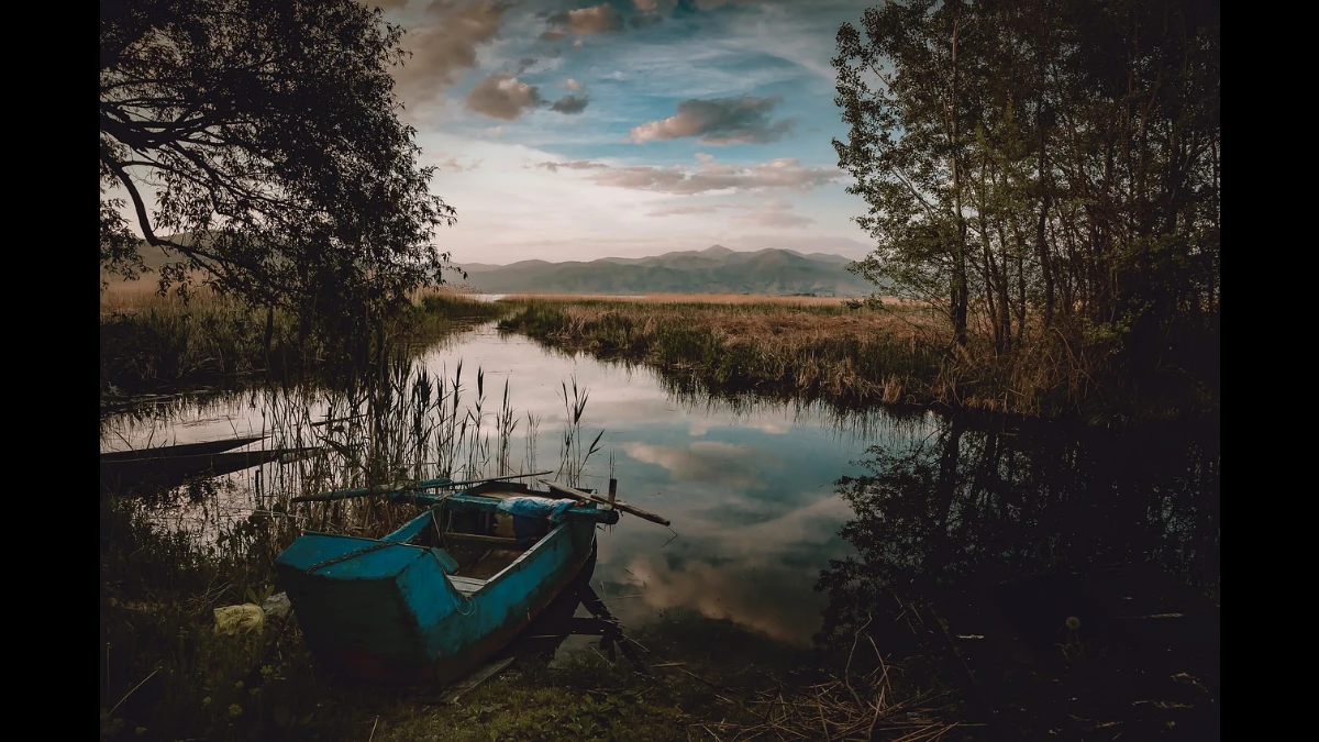 La sera scende sull'acqua di un lago. A riva la barca di un pescatore
