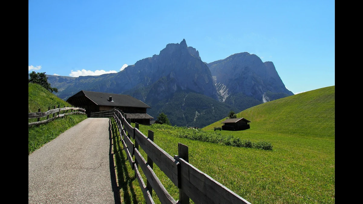 Un largo sentiero porta a una baita. Sullo sfondo alte montagne