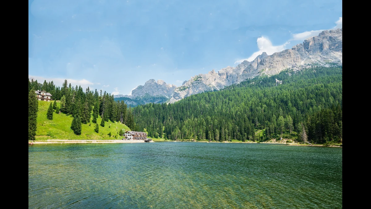 Lago alpino circondato da boschi di alte conifere e rocce scoscese