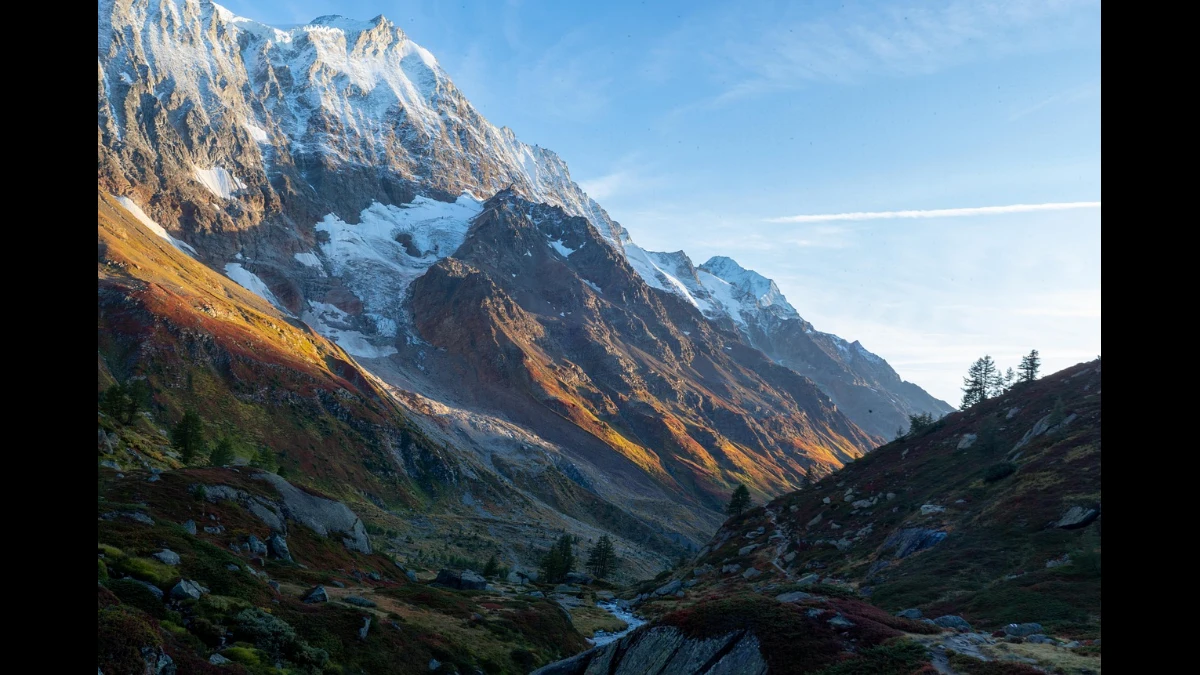 Alba in autunno. Il sole accende i colori degli ultimi prati e delle rocce. In ombra in basso un piccolo torrente