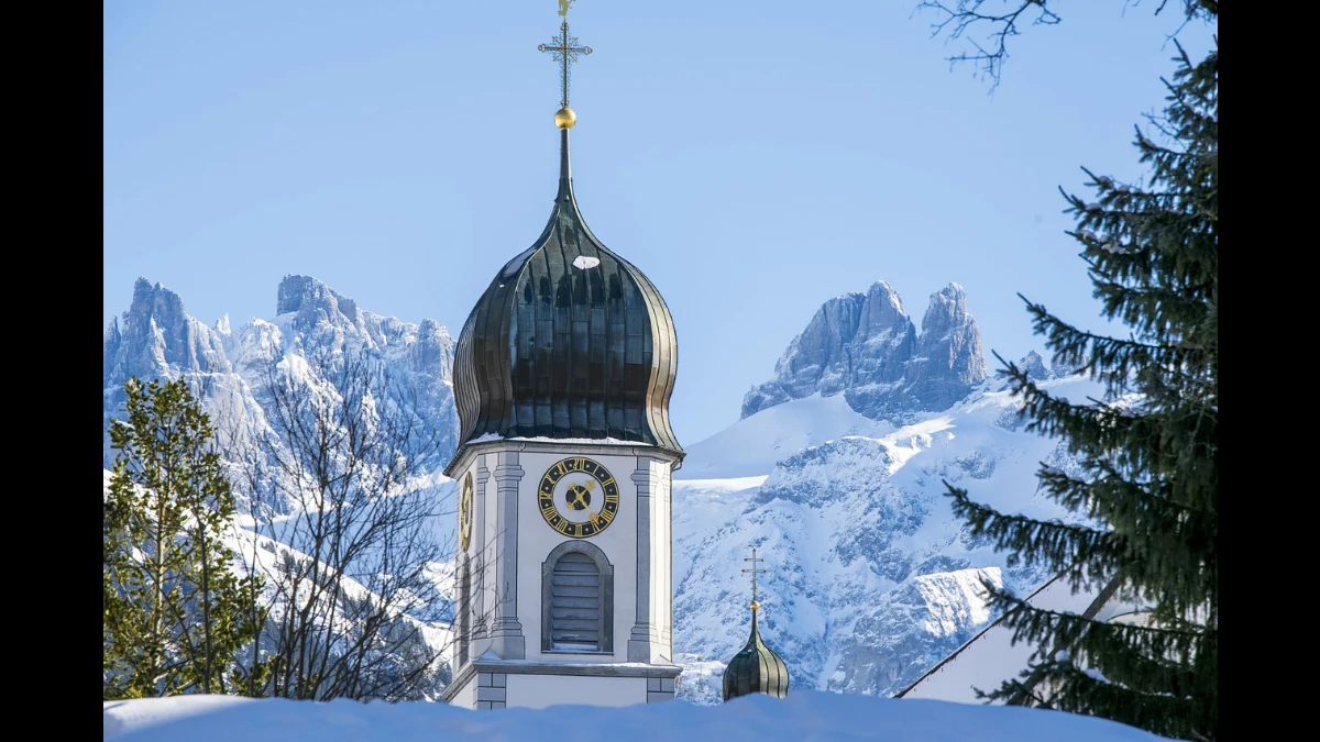 Dietro al campanile sta un cielo azzurro e che di montagne ricoperte di neve